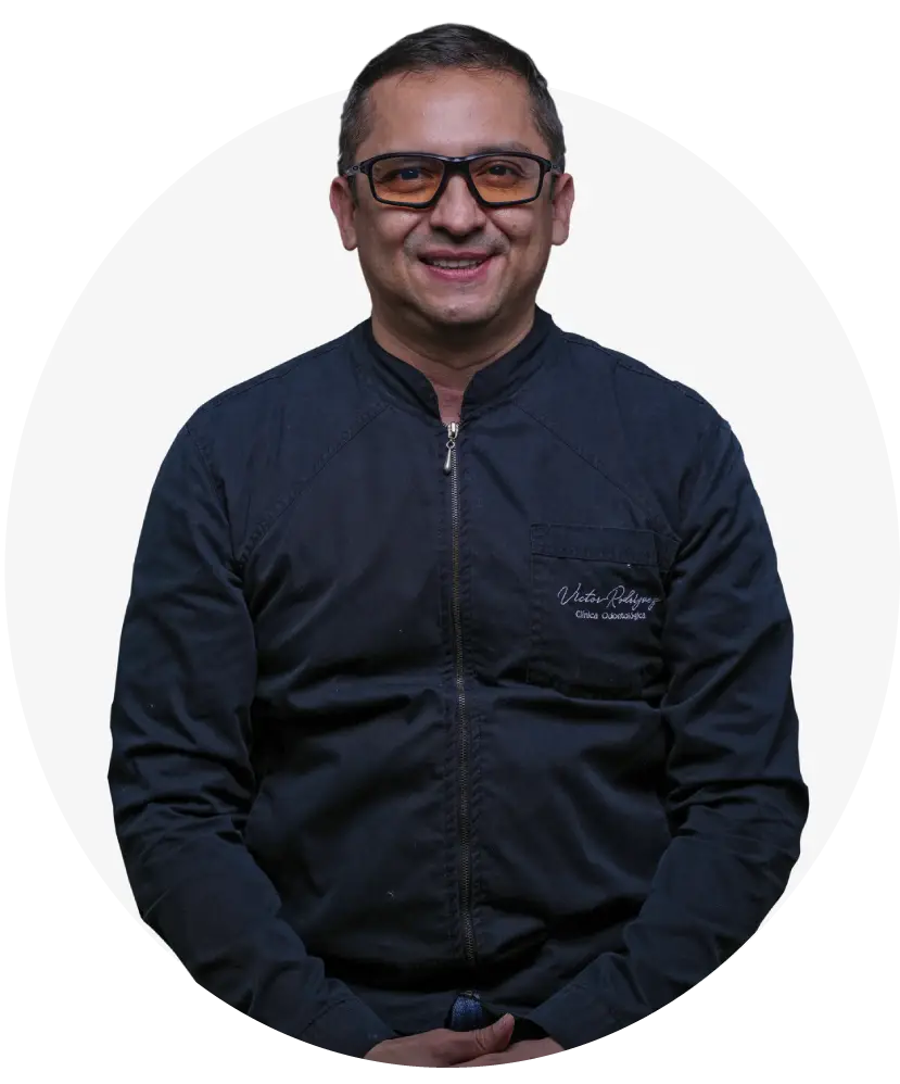Dr. Víctor Rodríguez, odontólogo especialista, posando con uniforme clínico frente al logo de su clínica odontológica en Bucaramanga.